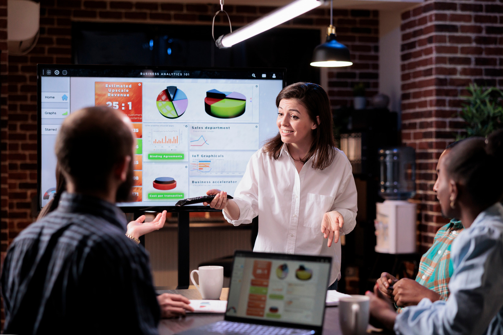 Marketing 1 smiling caucasian woman startup office doing business presentation big tv screen with charts front team confident employee presenting growing sales statistics late night meeting small